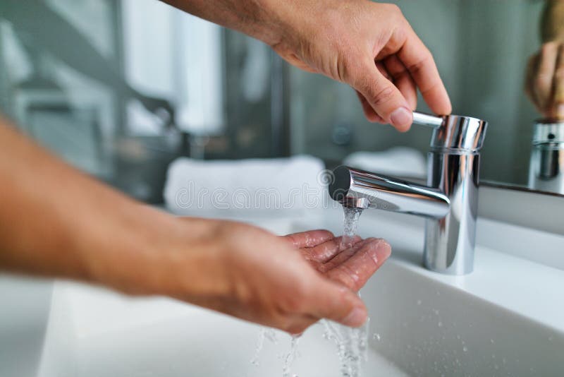 Man washing hands in bathroom sink at home checking temperature touching running water with hand. Closeup on fingers