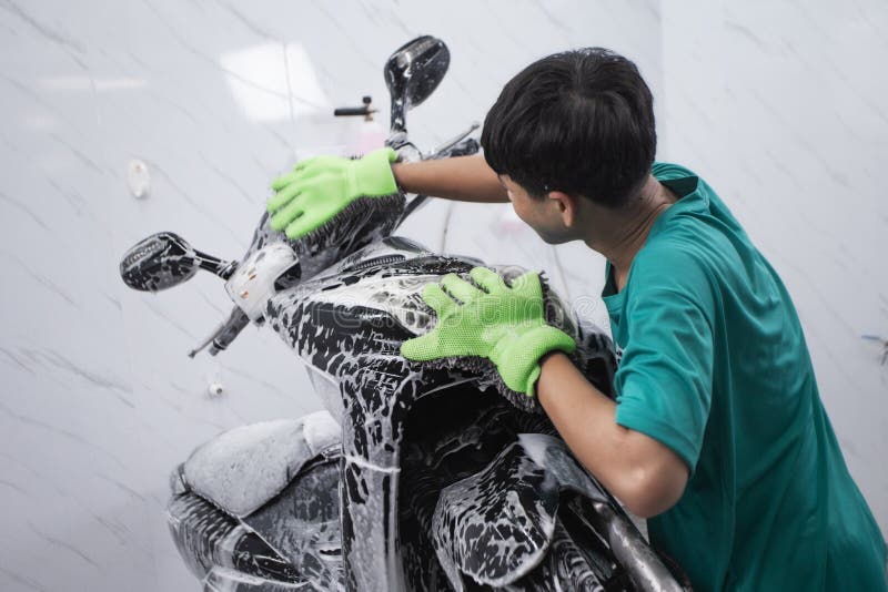 Man Washing His Motorcycle or Scooter with Soap and Sponge Stock Image
