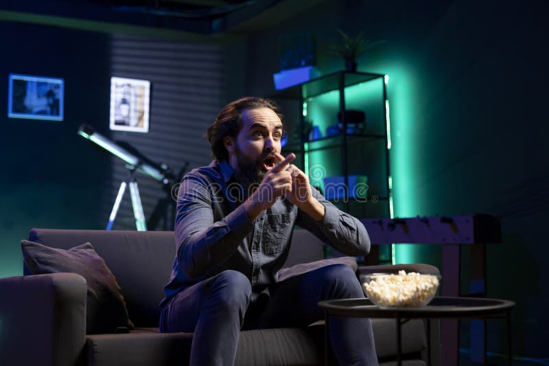 Man watching shows on TV, eating popcorn, reacting with surprise to plot twist royalty free stock image