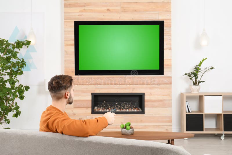 Man watching TV on sofa in living room with decorative fireplace. Man watching TV on sofa in living room with decorative fireplace