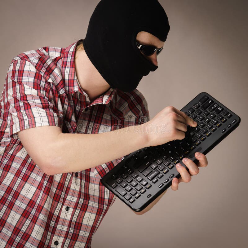 Man wearing balaclava holding keyboard stock photos