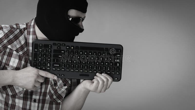 Man wearing balaclava holding keyboard stock photo