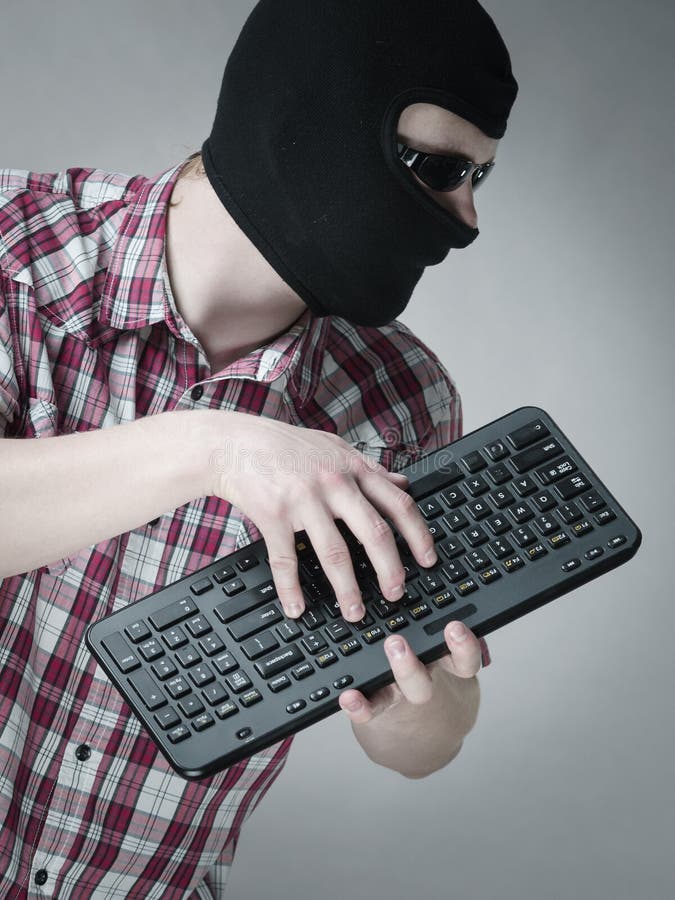 Man wearing balaclava holding keyboard stock photos