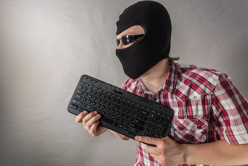 Man wearing balaclava shooting from keyboard. Crazy hacker man. Unrecognizable guy wearing black balaclava pretending to shoot with computer keyboard. Hate speech on the internet