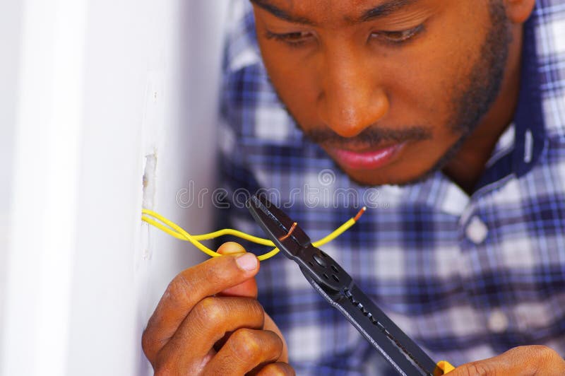Man wearing white and blue shirt working on electrical wall socket wires using screwdriver, electrician concept stock images