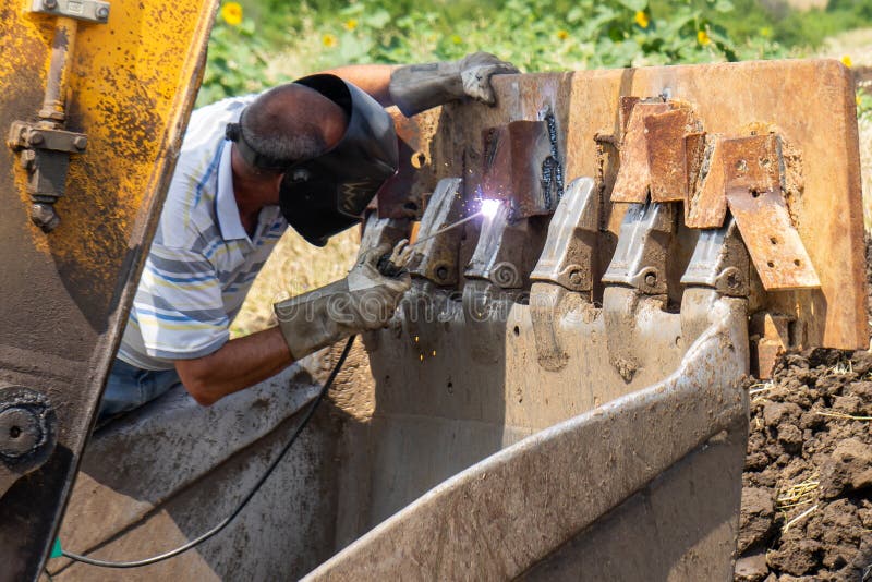 Man Welding an Excavator Bucket Outdoors Stock Photo Image of field