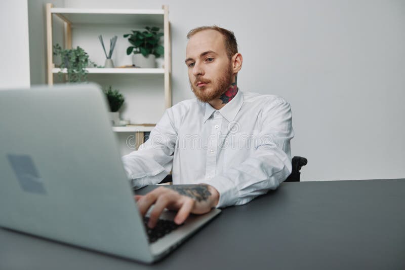 Young tattooed businessman looking at camera while working with laptop at  workplace  Stock Photo  Dissolve