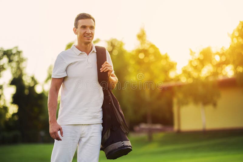 A man in a white suit walks the golf course with a bag of golf clubs against a beautiful sunset stock image A man in a white suit walks the golf course with a bag of golf clubs against a beautiful sunset stock image