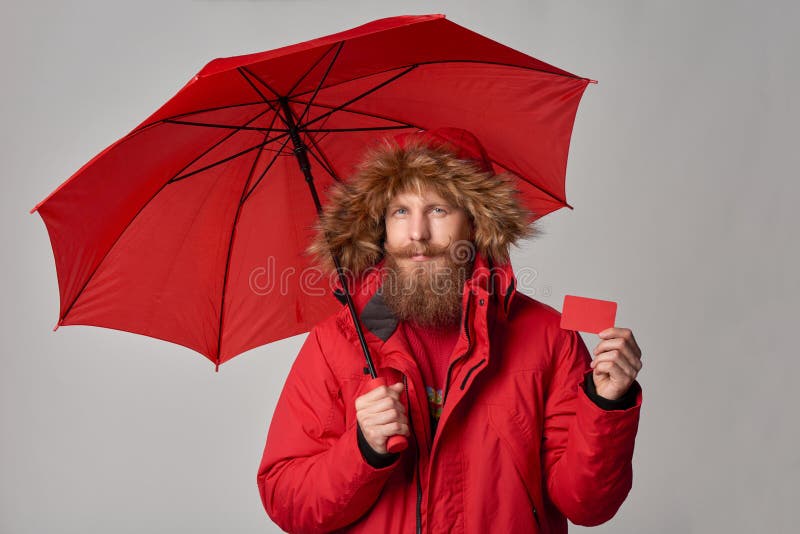 Man in winter jacket with umbrella showing blank credit card