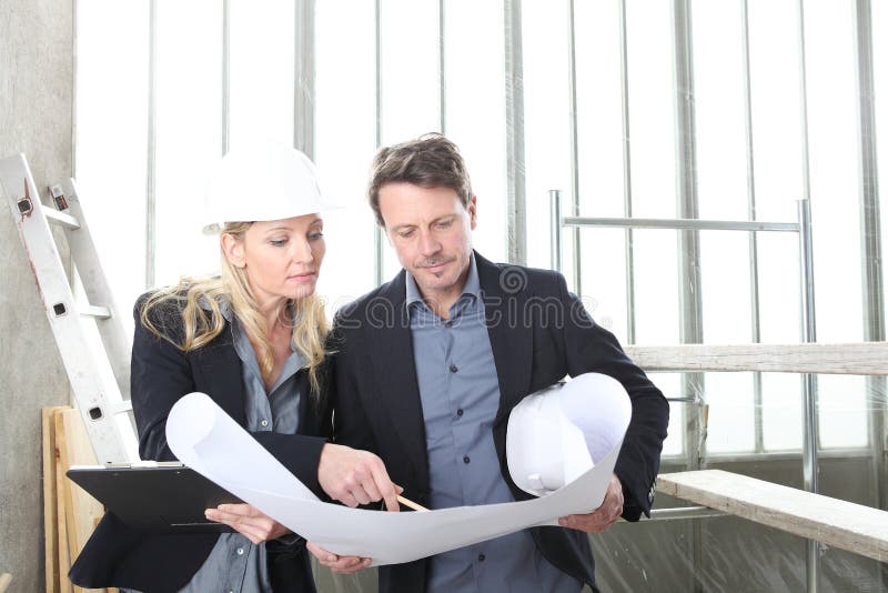 Man and woman architects or engineers work together discussing with blueprint in the inside the construction building site royalty free stock photography