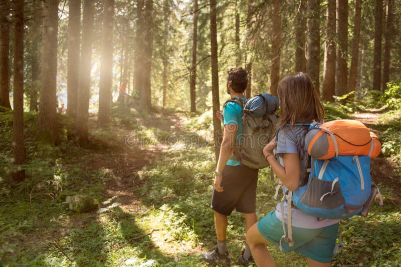 Man and woman with backpack walking on hiking trail path in forest woods during sunny day.Group of friends people summer