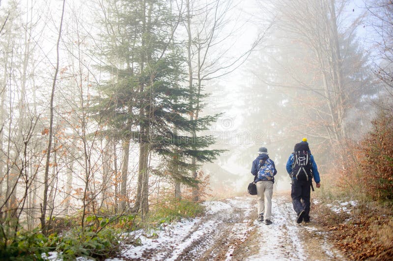 Man and woman backpackers hiking on foggy forest mountain trail