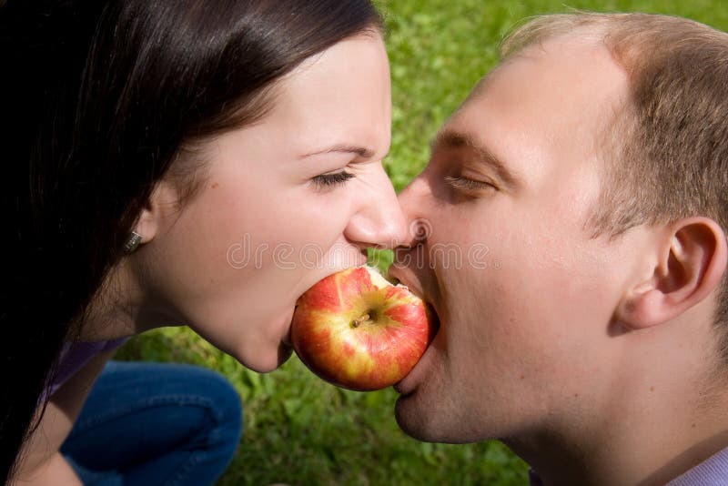 Man and woman bite a red apple