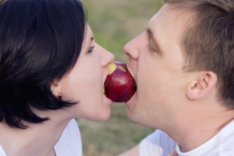 Man and woman bite a red apple