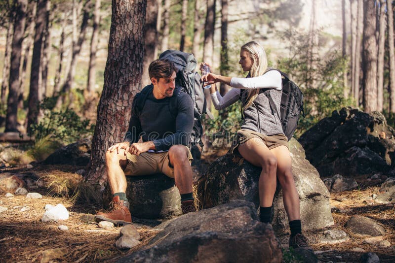 Man and woman hikers relaxing while trekking in forest. Hiker couple taking a break sitting on rock and drinking water. Man and woman hikers relaxing while trekking in forest. Hiker couple taking a break sitting on rock and drinking water.