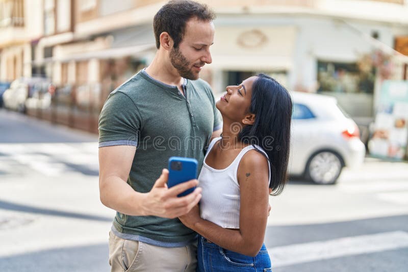 Man And Woman Interracial Couple Hugging Each Other Using Smartphone At 