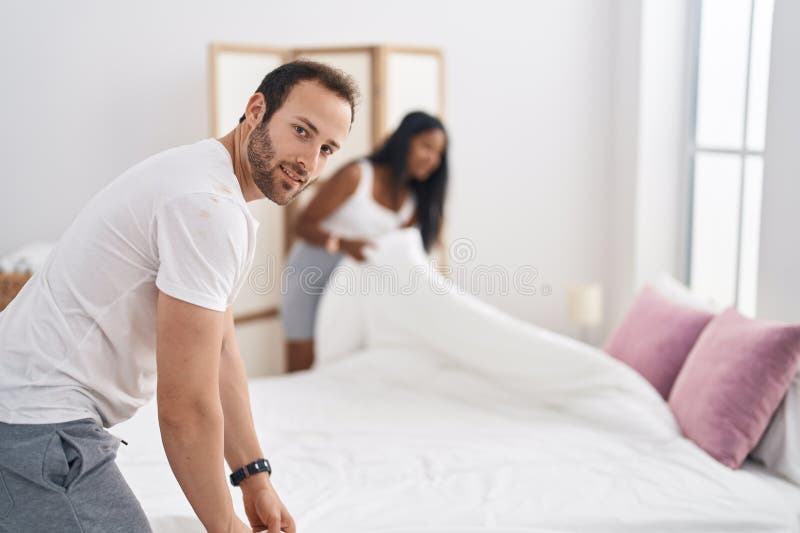 Man and Woman Interracial Couple Making Bed at Bedroom Stock Photo