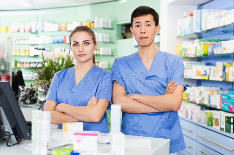 Efficient serious man and woman pharmacists are posing near table with cashbow in apothecary.