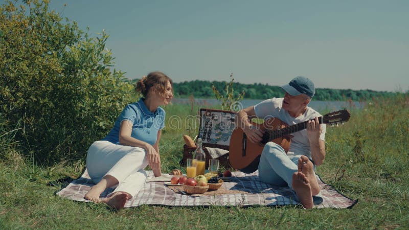 A man and a woman relax on a picnic with a guitar.