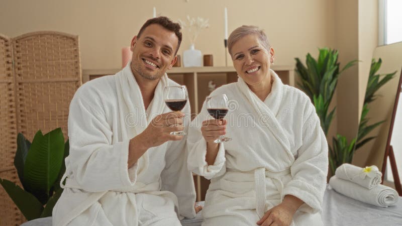 Man and woman in white bathrobes enjoy a relaxing spa experience with red wine inside a cozy wellness center, displaying happiness and bonding. Pampering experience stock images, royalty-free photos and pictures