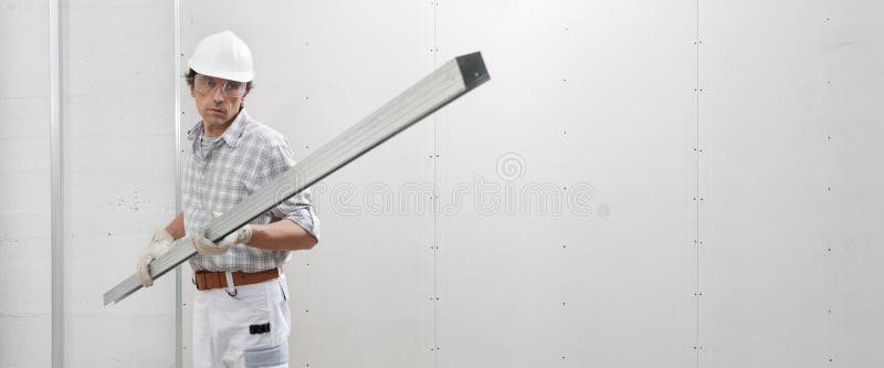 Man worker with drywall metal profile for installing plasterboard sheet to wall. Wearing white hardhat, work gloves and safety