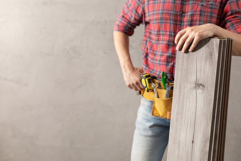 Man worker holding  laminate floor plank and tool belt . Male hand and construction tools