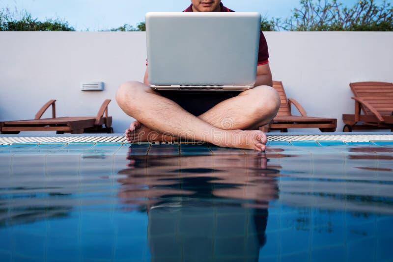 A man working on laptop computer, sitting at poolside, selective focus