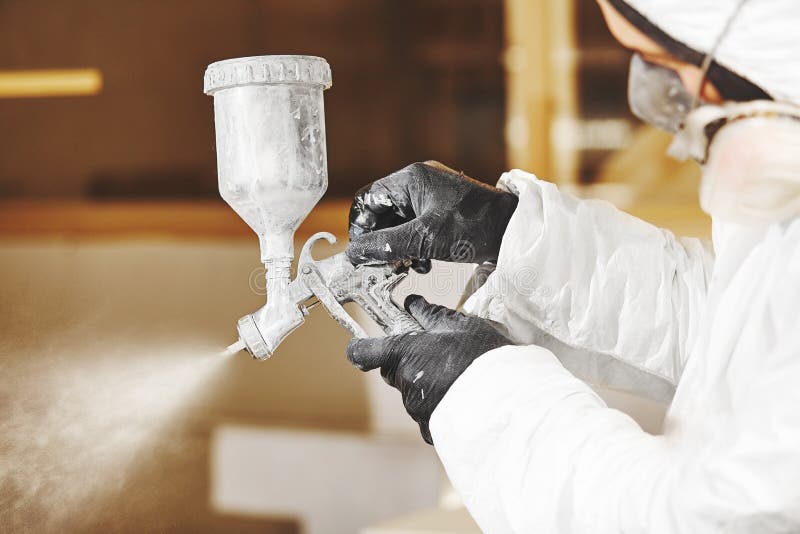 Man working with paint spray gun, airless spraying to wood. Worker wears a respirator in the paint shop.