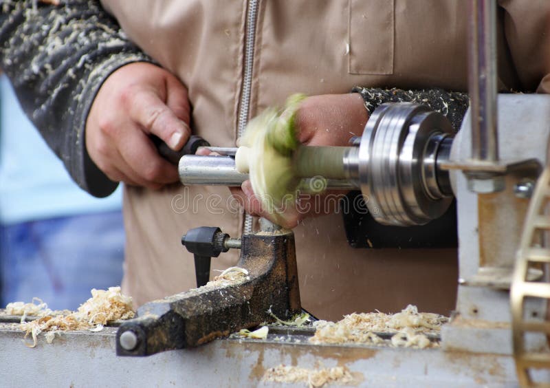 A closeup view of a workman using a wood lathe to fashion a finished wood product. A closeup view of a workman using a wood lathe to fashion a finished wood product.