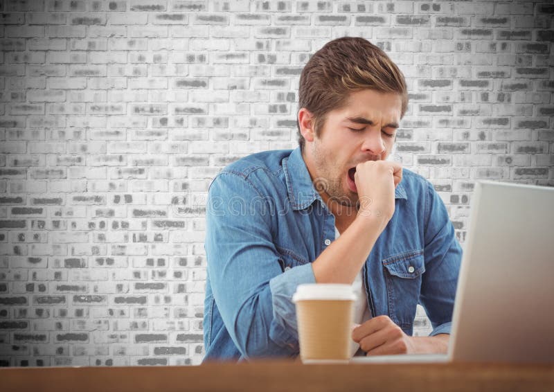 Man Yawning while Using Laptop in Office Against Brick Wall in