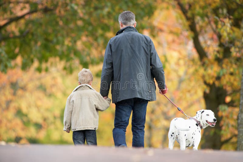 Man With Young Son Walking Dog Through Park