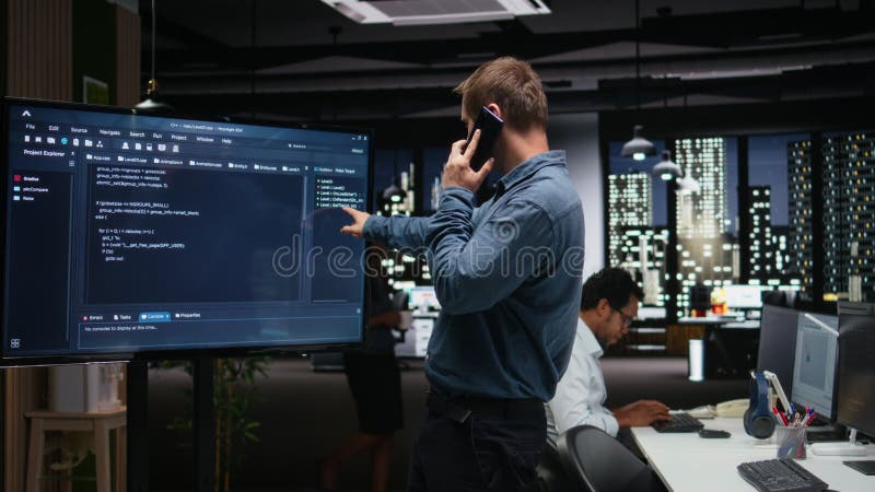 Manager analyzes code on screen, makes phone call stock video footage