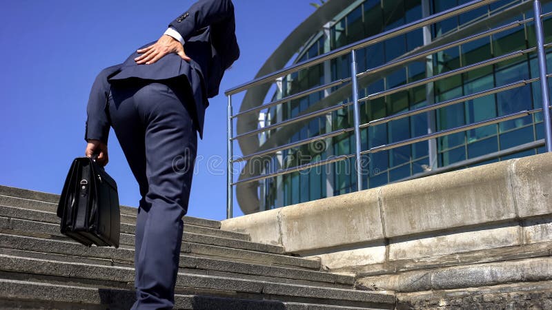 Manager in suit suffering from lower back pain, slipped disc, disease symptom, stock photo