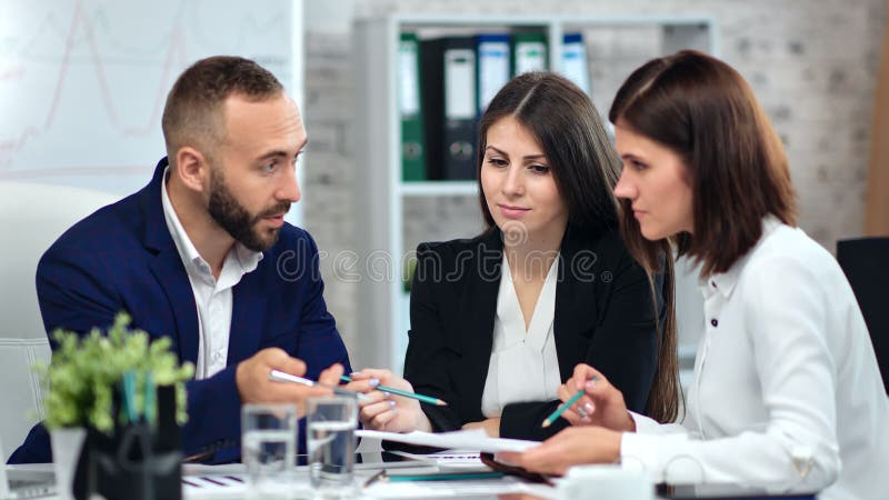 Manale trendy baas in het pak, die met twee vrouwelijke werknemers in het moderne kantoorinterieur praat