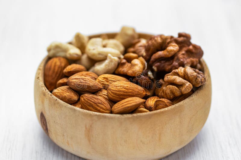 Mandorle, castagne e noci in una ciotola di legno marrone su uno sfondo di legno bianco fotografia stock libera da diritti Mandorle, castagne e noci in una ciotola di legno marrone su uno sfondo di legno bianco fotografia stock libera da diritti