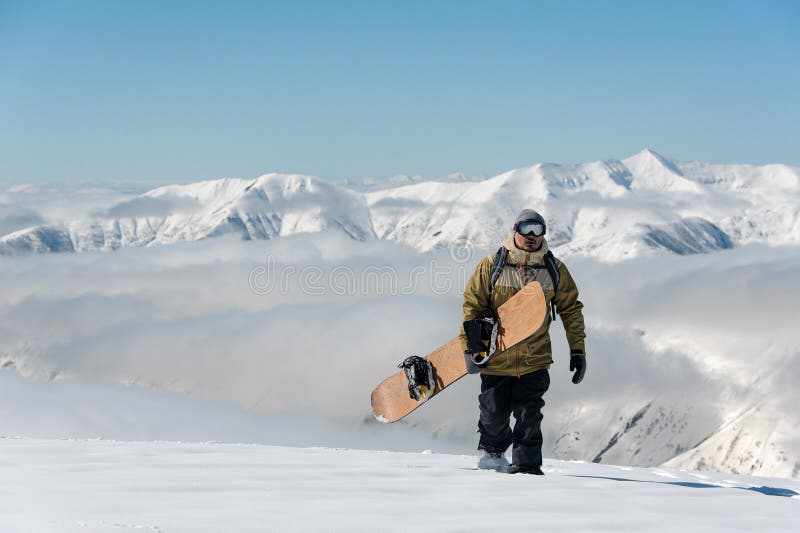 Manful snowboarder идя с коричневым сноубордом в держателе стоковое фото Manful snowboarder идя с коричневым сноубордом в держателе стоковое фото