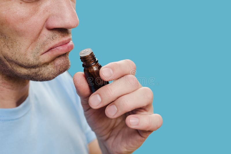 Sad sick man with smell blindness sniffing bottle of essential oil. Smell loss screening: Medical practitioner administers anosmia test. Sad sick man with smell blindness sniffing bottle of essential oil. Smell loss screening: Medical practitioner administers anosmia test