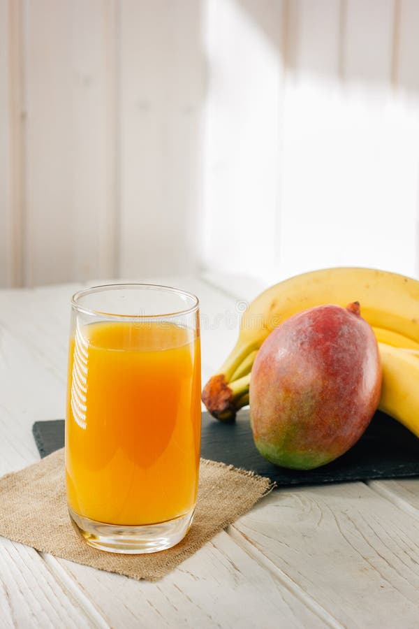 Mango and Banana Juice in Glass Over White Wooden Table. Stock Photo