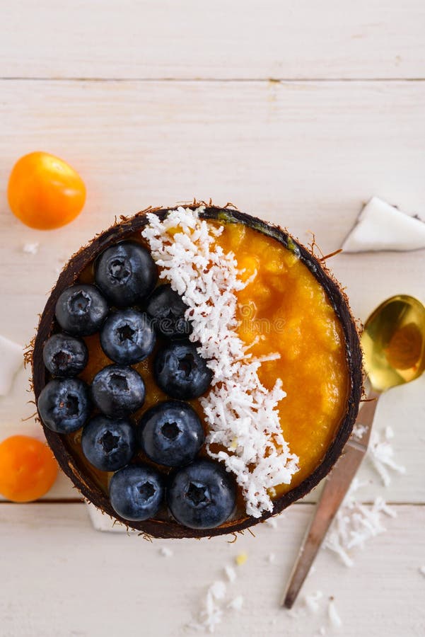 Mango Dessert with Blueberries, Coconut Chips in Coconut Bowl on White Background, Smoothie Bowl