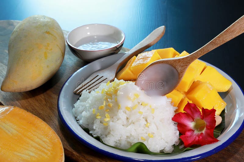 Mango sticky rice with wooden spoon pouring coconut milk in the white plate on wooden table background. Famous Dessert in Thailand royalty free stock image Mango sticky rice with wooden spoon pouring coconut milk in the white plate on wooden table background. Famous Dessert in Thailand royalty free stock image