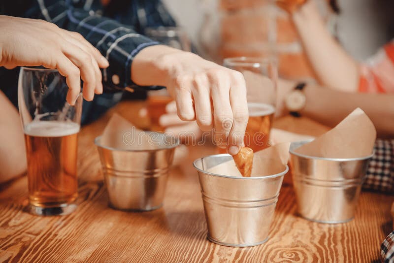 Manhanden tar mellanmålsmällare, krutonger med sås och drinköl i barstång på trätabellen royaltyfri foto Manhanden tar mellanmålsmällare, krutonger med sås och drinköl i barstång på trätabellen royaltyfri foto