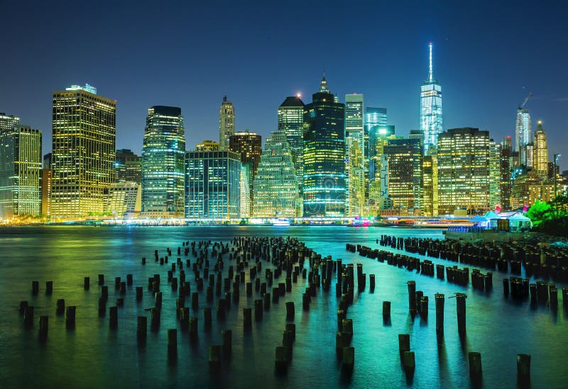 Illuminated skyline of New York City at night reflected in waters with wood pylons from Brooklyn, USA. Illuminated skyline of New York City at night reflected in waters with wood pylons from Brooklyn, USA.