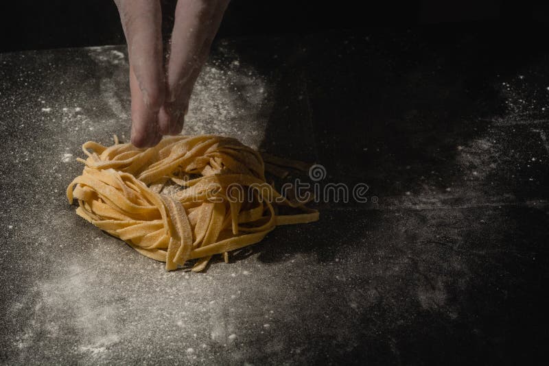 Mani del cuoco unico che fanno gli spaghetti, pasta, tagliatelle con pasta fresca sulla tavola nera con immagini stock libere da diritti Mani del cuoco unico che fanno gli spaghetti, pasta, tagliatelle con pasta fresca sulla tavola nera con immagini stock libere da diritti