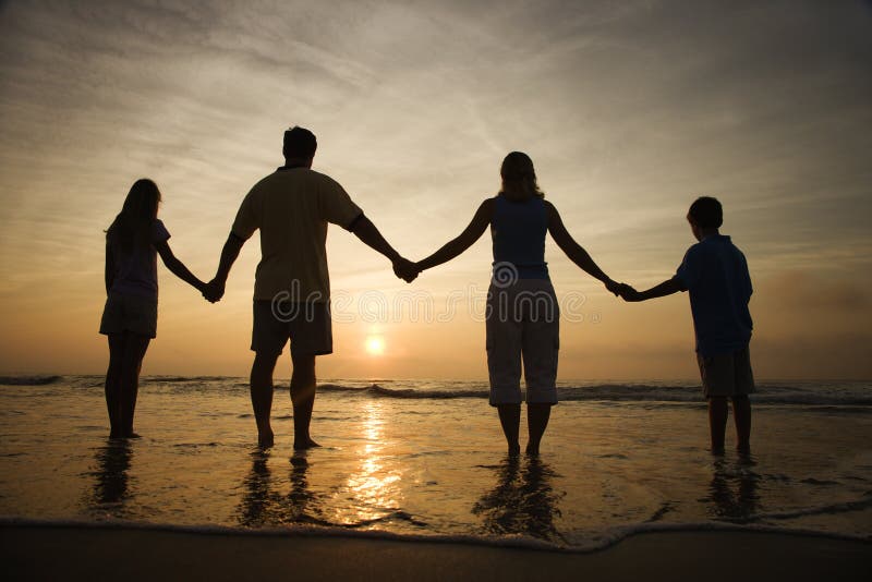 Mani della holding della famiglia sulla spiaggia che guarda tramonto
