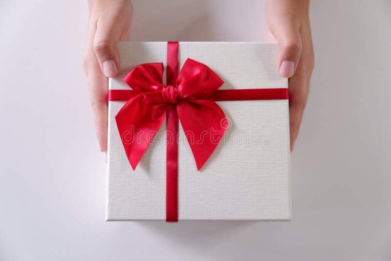 Mani delle donne del primo piano che inviano il contenitore di regalo bianco con il nastro rosso su fondo bianco immagini stock Mani delle donne del primo piano che inviano il contenitore di regalo bianco con il nastro rosso su fondo bianco immagini stock