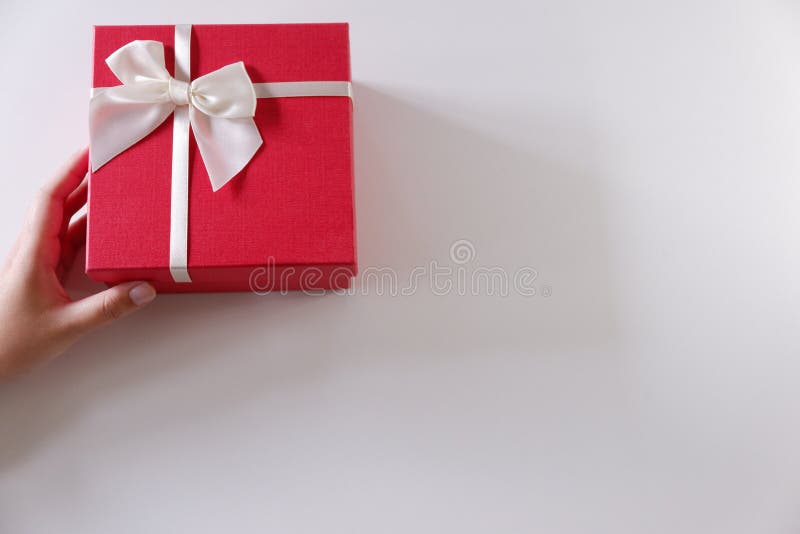Mani delle donne del primo piano che inviano il contenitore di regalo rosso con il nastro bianco su fondo bianco immagine stock libera da diritti Mani delle donne del primo piano che inviano il contenitore di regalo rosso con il nastro bianco su fondo bianco immagine stock libera da diritti