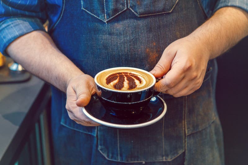 Mani di barista che tengono il cappuccino nero della tazza di caffè con il segno di logo della squadra di pallacanestro di Toront fotografia stock libera da diritti Mani di barista che tengono il cappuccino nero della tazza di caffè con il segno di logo della squadra di pallacanestro di Toront fotografia stock libera da diritti