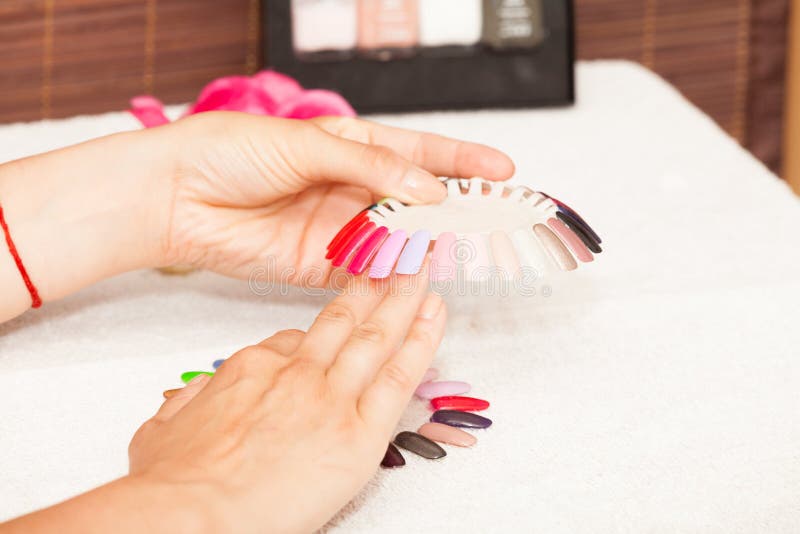 Mani di una donna che sceglie il colore dello smalto per unghie immagine stock libera da diritti Mani di una donna che sceglie il colore dello smalto per unghie immagine stock libera da diritti