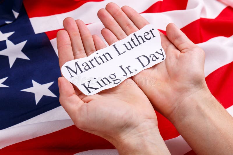 Mani di una tenuta dell'uomo sull'iscrizione Martin Luther King Jr delle palme giorno Contro lo sfondo della bandiera americana fotografia stock libera da diritti Mani di una tenuta dell'uomo sull'iscrizione Martin Luther King Jr delle palme giorno Contro lo sfondo della bandiera americana fotografia stock libera da diritti