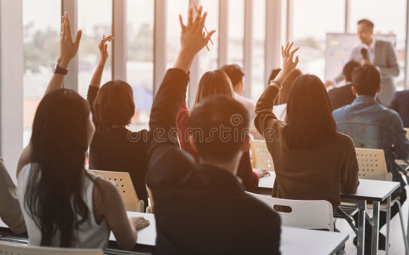 Mani e braccia su sollevati di grande gruppo nella stanza di classe di seminario essere d'accordo con l'altoparlante alla sala ri
